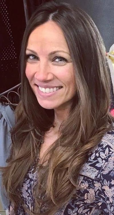 Smiling woman with long brown hair and floral patterned top.