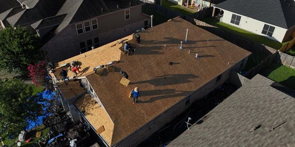 Workers installing new roofing on a residential house under clear sunlight.