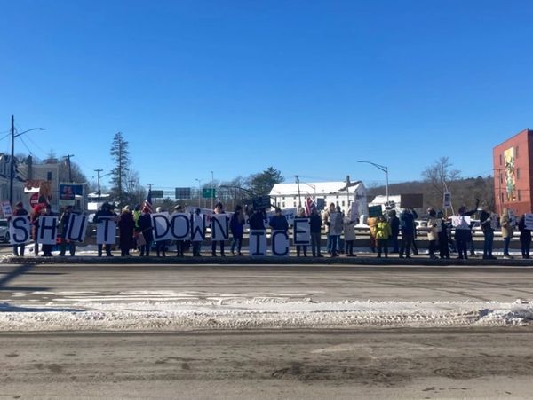 Protesters holding signs saying 'SHUT DOWN ICE' on a snowy street.