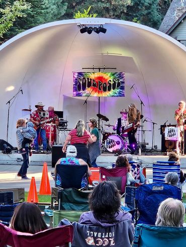 Outdoor concert with band and audience enjoying music in lawn chairs.