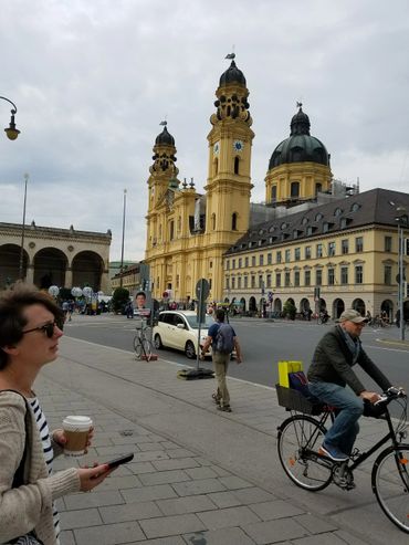 People walking and biking near a historic yellow church in a European city.