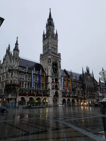 Gothic-style building with tall clock tower and flags on a rainy day.