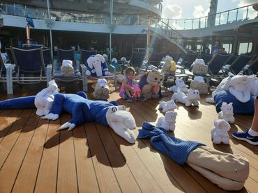 Child sitting among towel animals on a cruise ship deck.