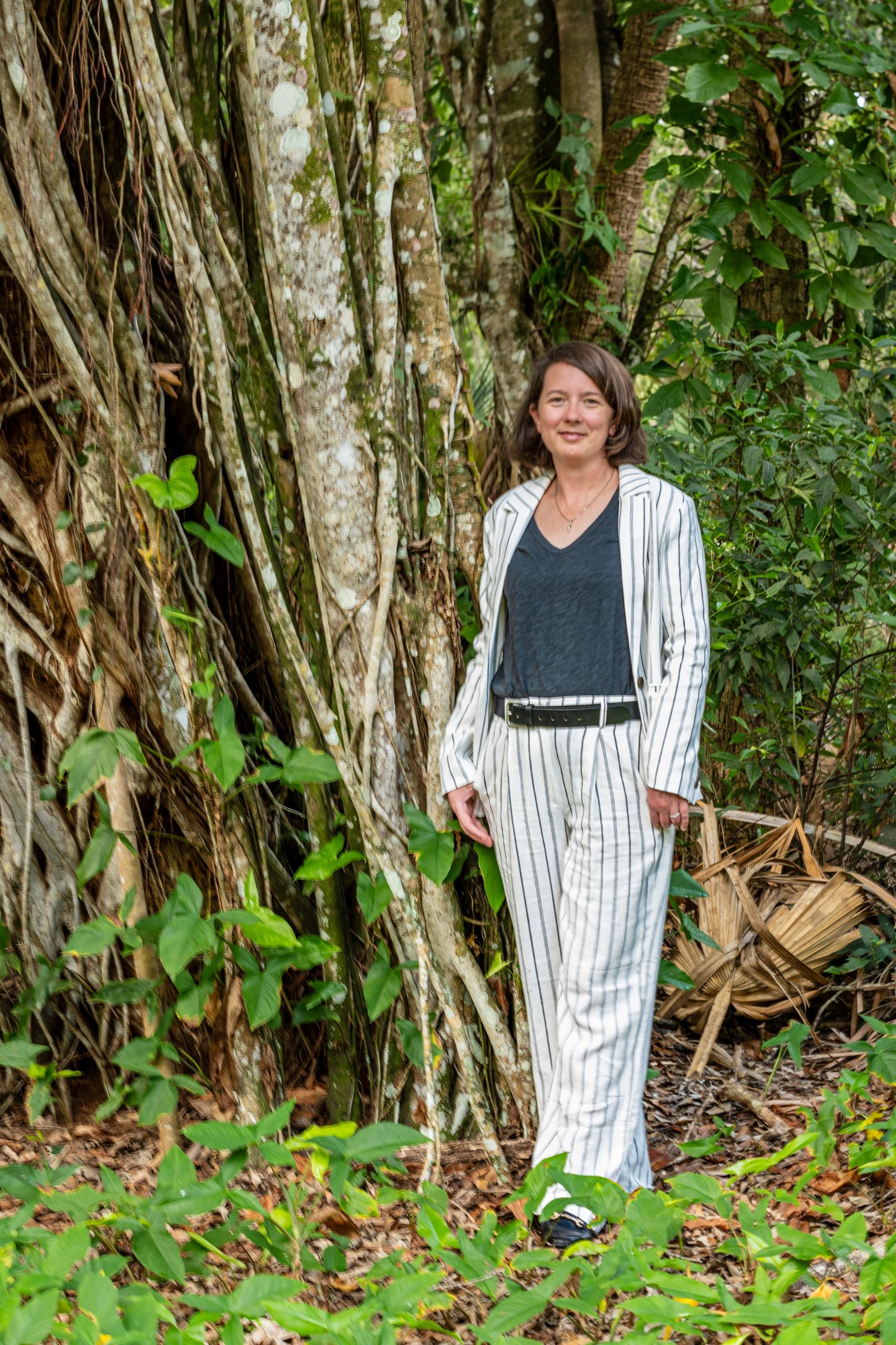 Woman in a white striped suit standing in a lush forest.