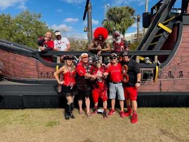 Group of people in red posing in front of a pirate ship backdrop outdoors.