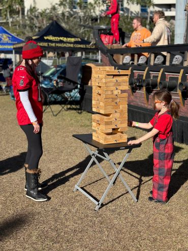 A woman and a girl play giant Jenga outdoors on a sunny day.