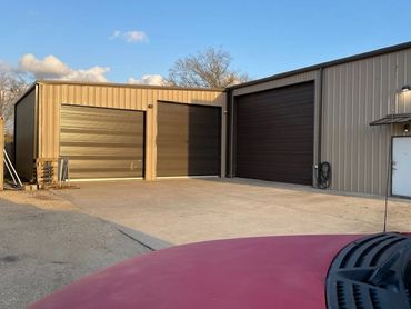 Industrial building with three large garage doors under clear sky.