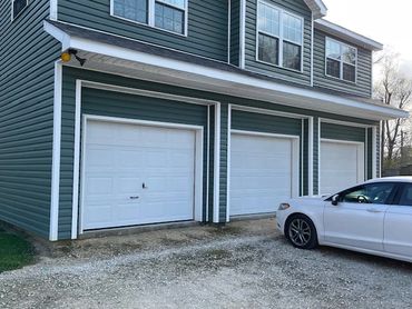 Three white garage doors on a blue house with a white car parked outside.