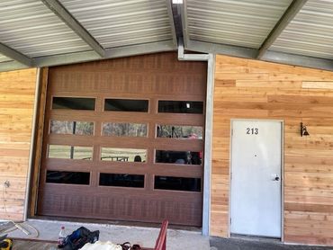 Wood-paneled building with a brown garage door and white door numbered 213.