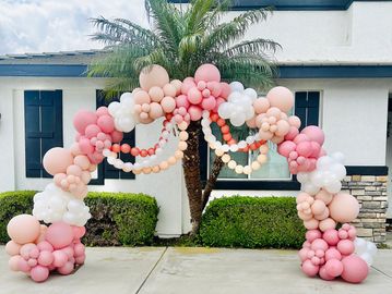 Colorful balloon arch in pink and white outside a house.