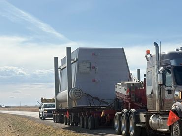 Oversized load truck transporting a large industrial structure on a highway.