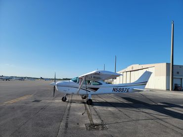 Small white airplane parked on an airport tarmac under a clear blue sky.