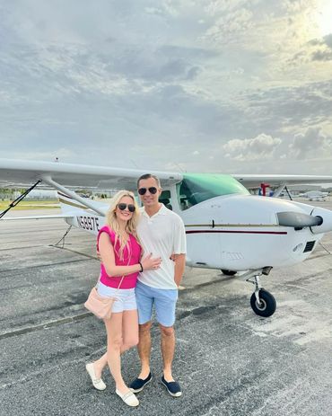 Couple posing in front of a small airplane on a sunny day.