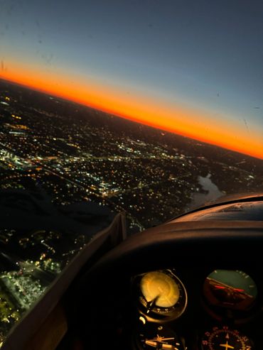 View of a city at sunset from an aircraft cockpit with illuminated instruments.