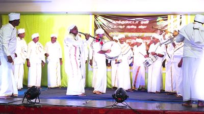 Men in traditional white attire performing a musical ceremony on stage.