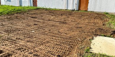 Freshly tilled soil in front of a white building with rusty doors.