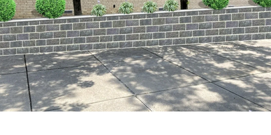 A stone wall with green round shrubs and a building with windows in the background.