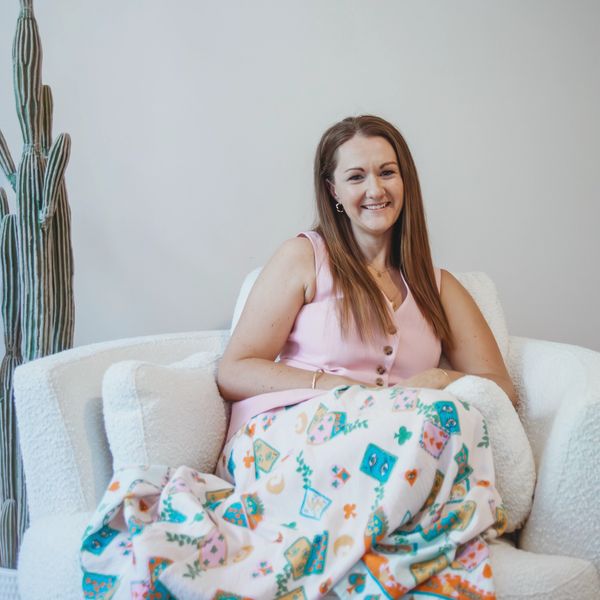 Smiling woman sitting on a white armchair with a patterned blanket.