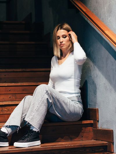 Woman sitting pensively on wooden stairs wearing casual clothes.