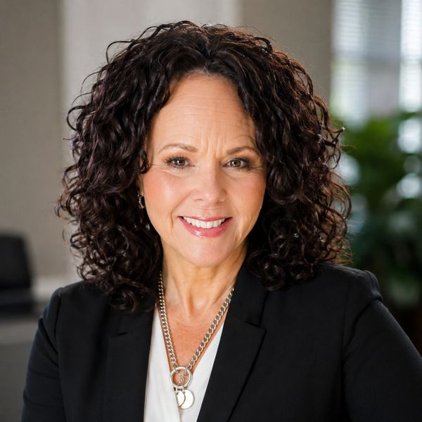 Confident woman with curly hair smiling warmly in a professional setting.