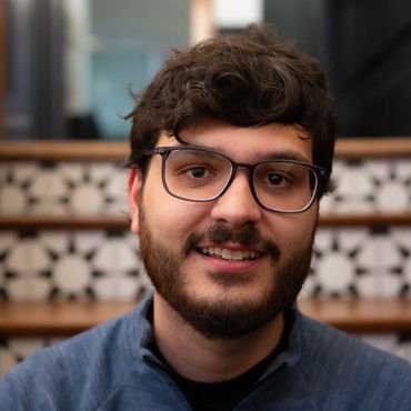 Young man with glasses smiling in front of decorative staircase.