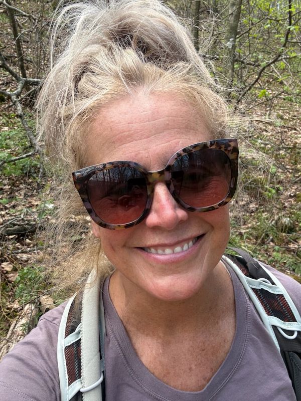 Smiling woman with sunglasses hiking outdoors.