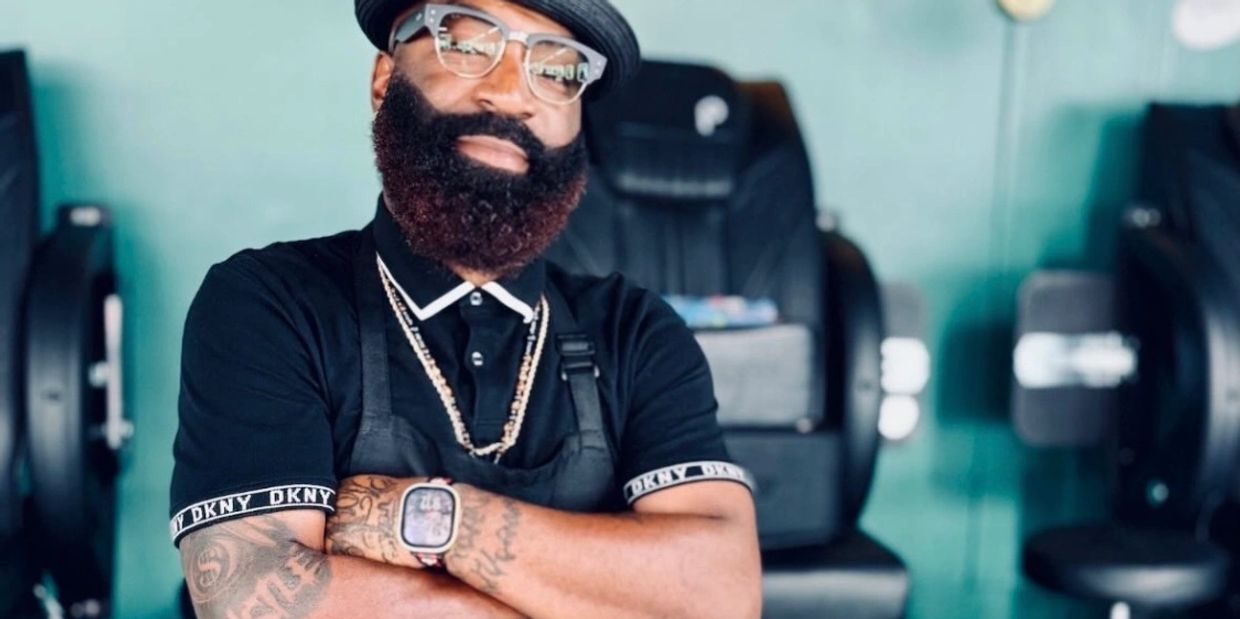 Man with beard and glasses posing confidently indoors.