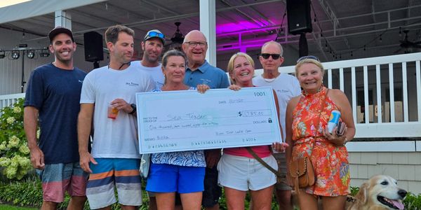 Group holding large check with a dog nearby.