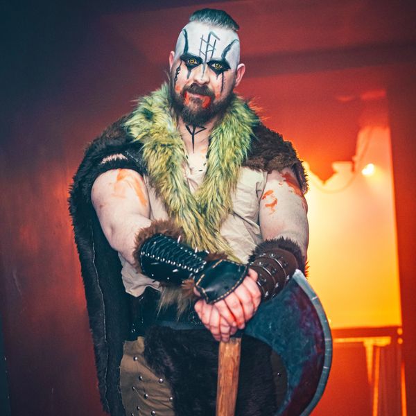 Man in Viking costume with face paint holding a battle axe.