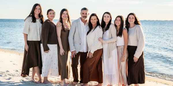 Family standing on the beach smiling at sunset.
