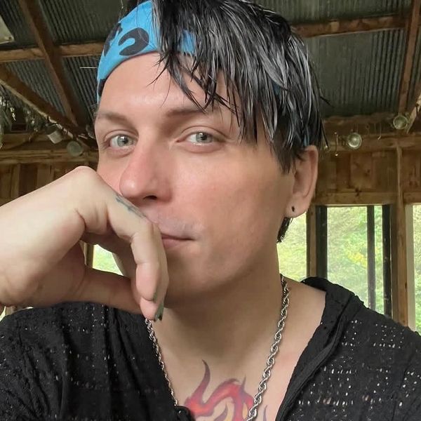 Man with blue bandana and chain necklace posing thoughtfully indoors.