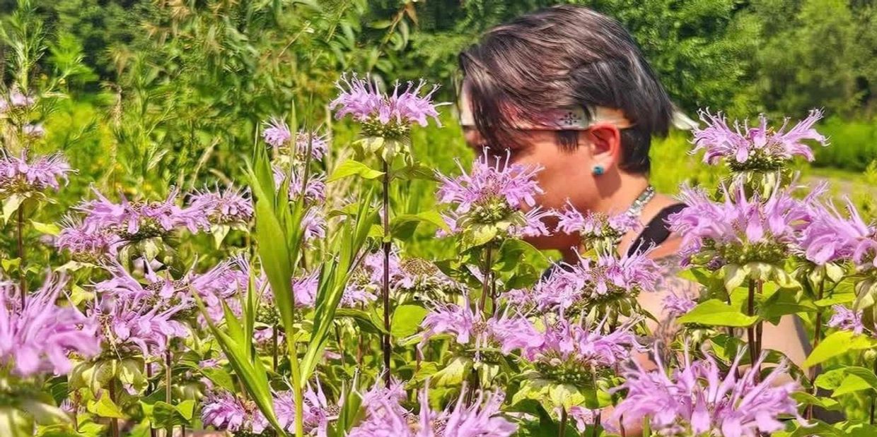 Person with short hair among vibrant purple flowers in a sunny garden.