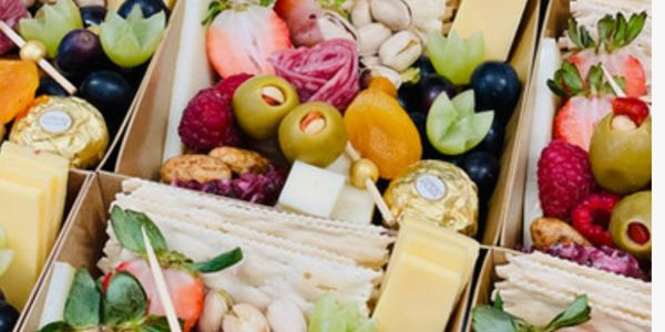 Assorted gourmet snack boxes with fruits, cheese, nuts, and chocolates.