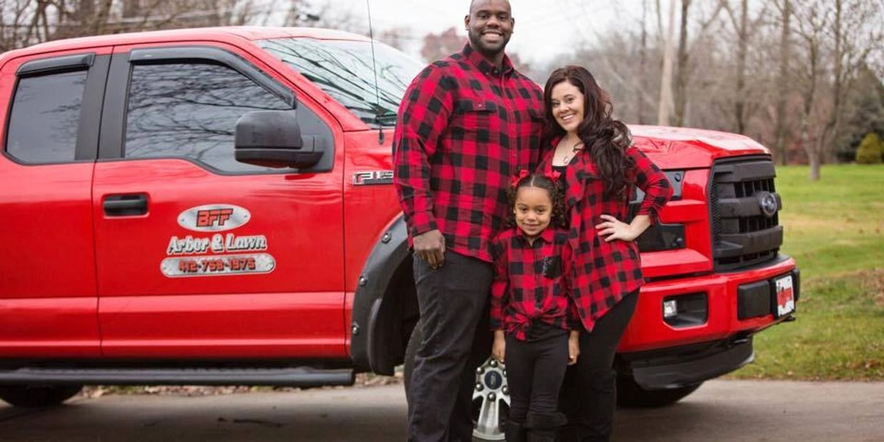 Family in matching red and black plaid shirts posing by a red truck.
