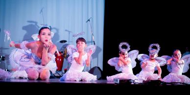 Young ballerinas in white costumes performing on stage.