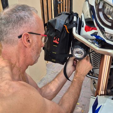 Man fixing a light on a motorcycle outdoors.