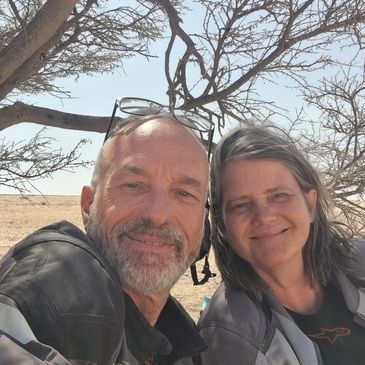 Smiling couple outdoors under a tree on a sunny day.