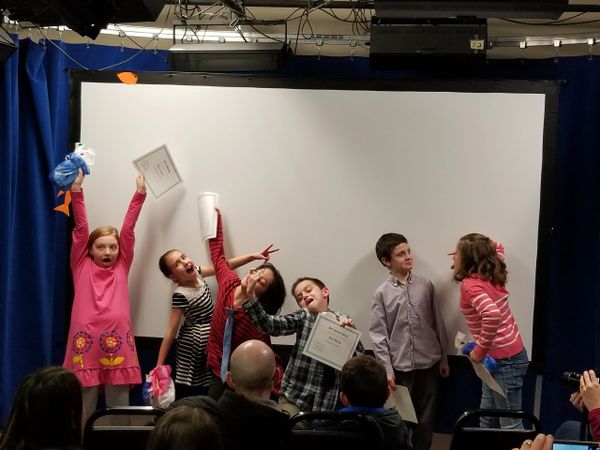 Group of kids making funny faces and holding award certificates in front of a projector screen