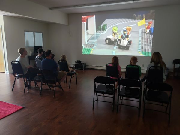 Kids and adults sitting audience style watching a lego movie projected on the wall.