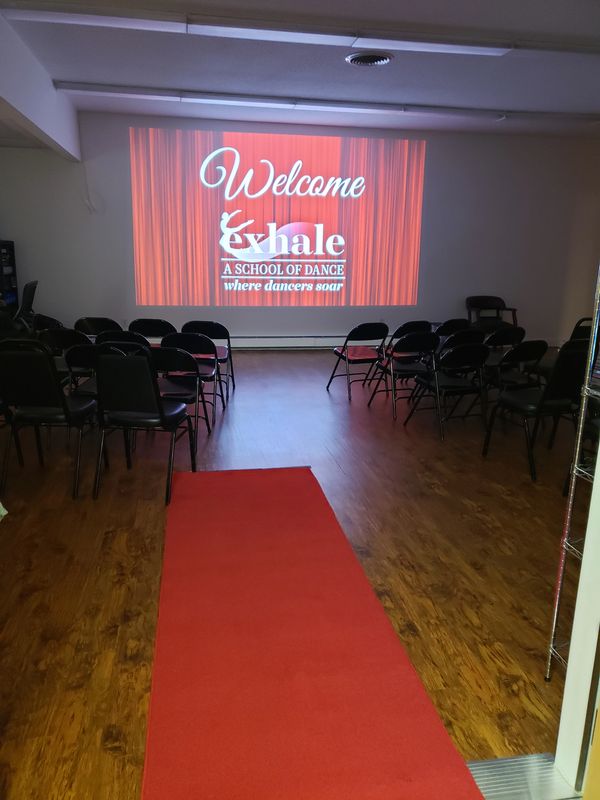 Red carpet with chairs set up audience style facing a projection that reads "Welcome Exhale"