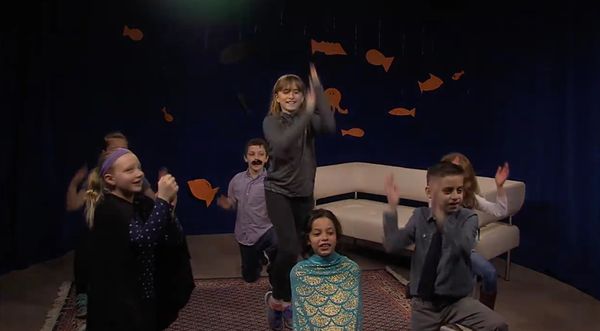 Group of kids performing a dance with paper fish in the background.