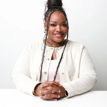 Confident woman with braided hair and white jacket smiling at the camera.