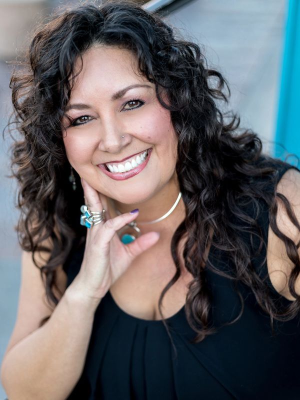 Smiling woman with curly hair and jewelry.