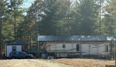 A Montana RV under a metal carport with a small shed and a parked car nearby.