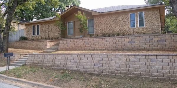 Single-story brick house with tiered retaining walls.