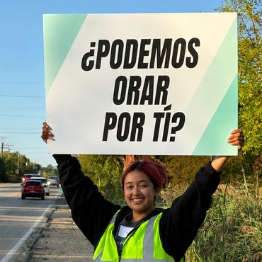 Young person holds a sign asking, 'Can we pray for you?' in Spanish.