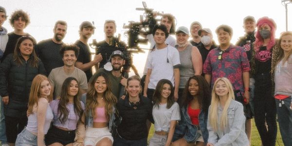A large diverse group posing outdoors, some holding camera equipment.