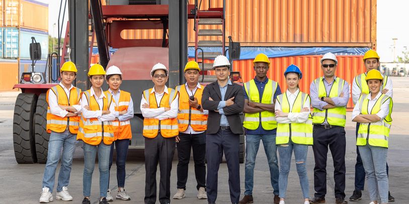 Diverse group of construction workers and engineers standing confidently at a shipping yard.
