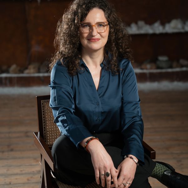 Woman with curly hair and glasses sitting confidently in a chair.