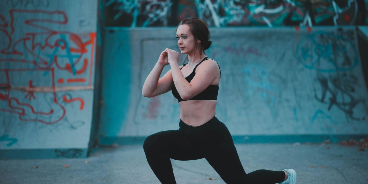 A women doing lunges in black athletic wear against graffiti background.